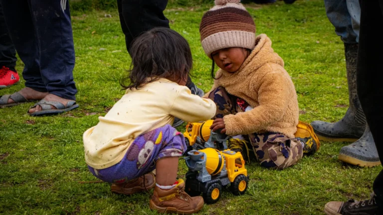 Dos niños pequeños juegan con camiones de juguete sobre el pasto