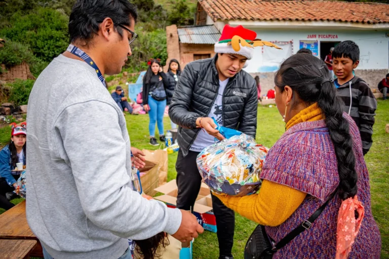Integrante de Cusco Creativos con gorro navideño entrega una canasta a una señora de la comunidad